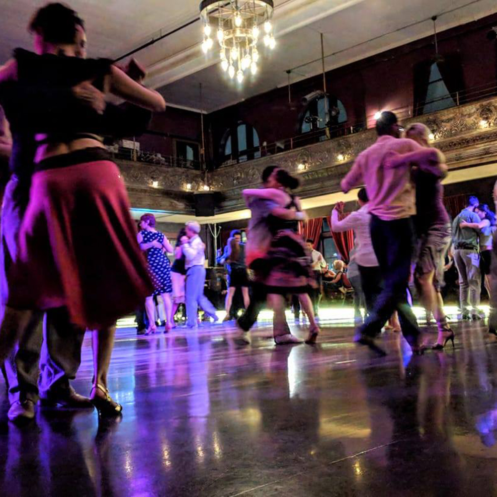 A low angle photo shows several couples tango dancing at Century Ballroom